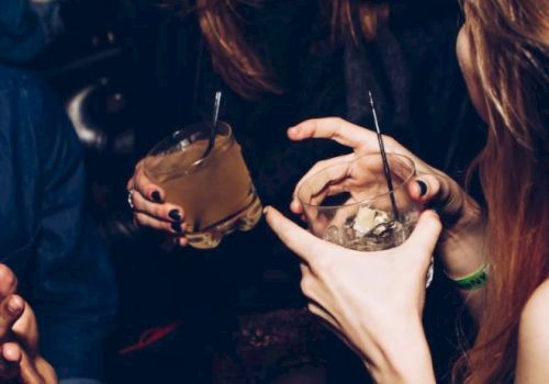 People are socializing in a dimly lit environment, holding cocktails and smiling, suggesting a lively and enjoyable atmosphere.
