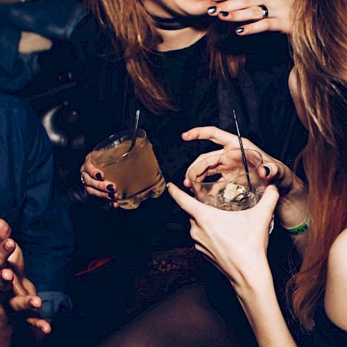 People are socializing in a dimly lit environment, holding cocktails and smiling, suggesting a lively and enjoyable atmosphere.