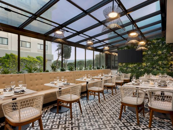 A modern restaurant with a glass roof, patterned floor tiles, and cozy seating arranged with tables set for dining.