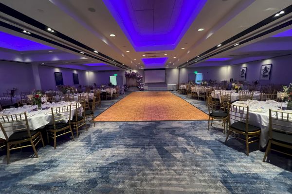 A formal event setting with round tables, chairs, and a central dance floor under purple ceiling lights, ready for a gathering.