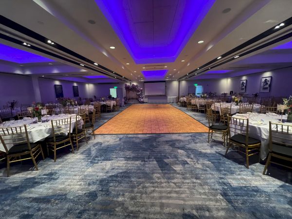 A formal event setting with round tables, chairs, and a central dance floor under purple ceiling lights, ready for a gathering.