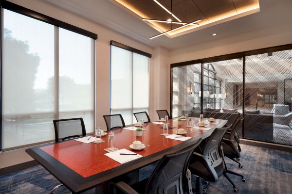 The image depicts a modern conference room with a long table, chairs, notepads, glasses, and cups, with frosted windows and contemporary lighting.