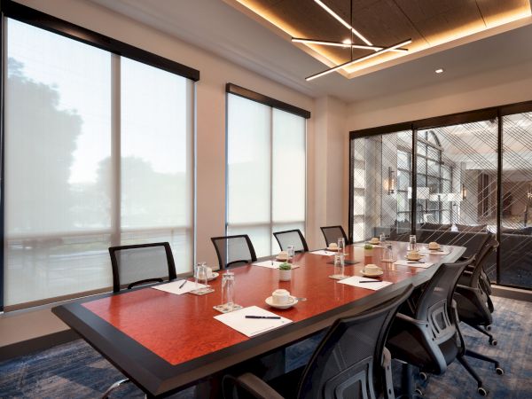 The image depicts a modern conference room with a long table, chairs, notepads, glasses, and cups, with frosted windows and contemporary lighting.