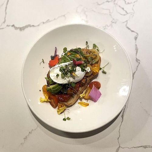 A plated open-face toast topped with creamy burrata, roasted veggies, mixed greens, and edible flowers and microgreens.