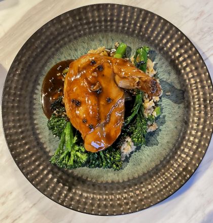 A glazed chicken piece over rice with steamed broccoli, topped with dark peppercorns and a rich orange sauce.
