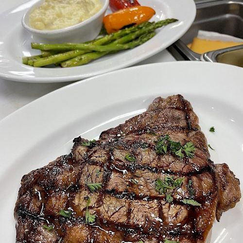 A plated grilled steak with herb sauce, plus asparagus, carrots, red pepper, and mashed potatoes for sides.