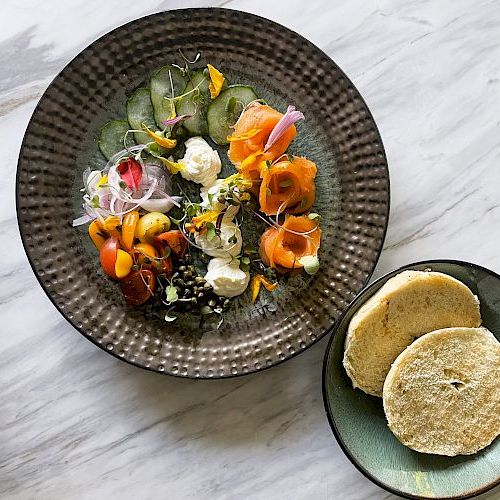 A plated salad of assorted cucumber, peppers, sprouts, and cheese with pita bread slices on the side.
