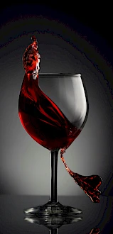 A wine glass with red liquid splashing upward, creatively resembling the shape of a bird atop the glass.