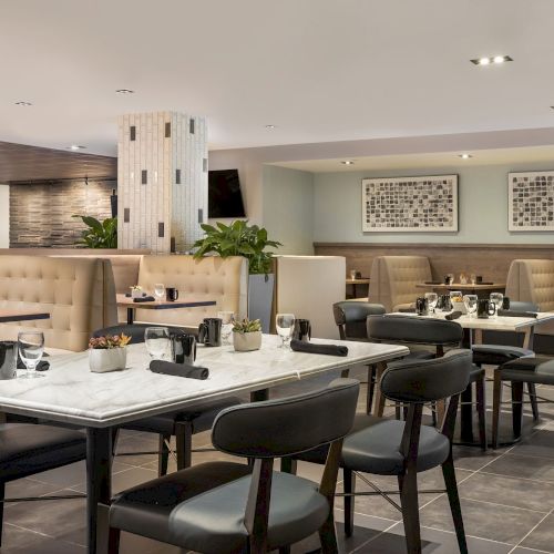 A modern dining lounge with neatly set tables, cushioned chairs, pendant lights, framed wall art, and a reception counter.