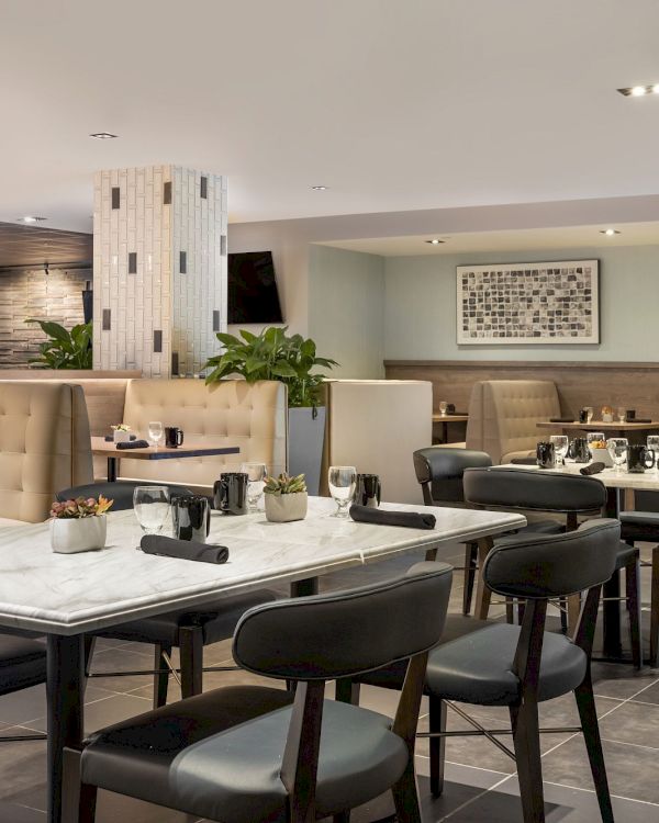 A modern dining lounge with neatly set tables, cushioned chairs, pendant lights, framed wall art, and a reception counter.