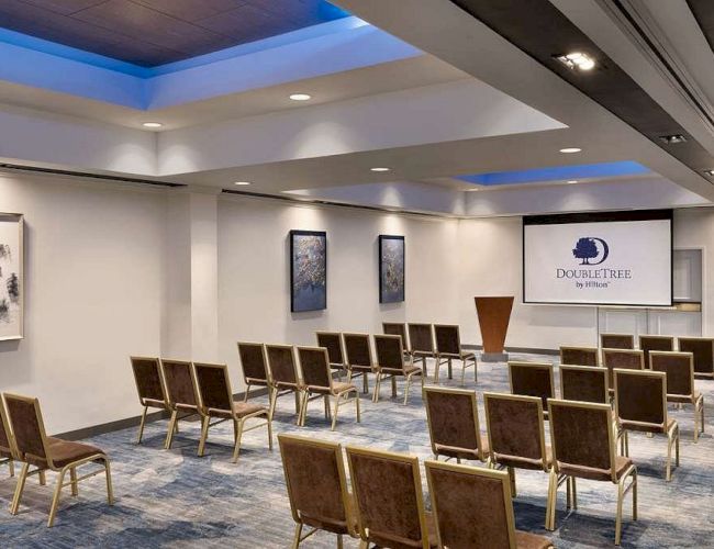A modern meeting room with rows of chairs, framed art, and a projection screen reading DoubleTree by Hilton.