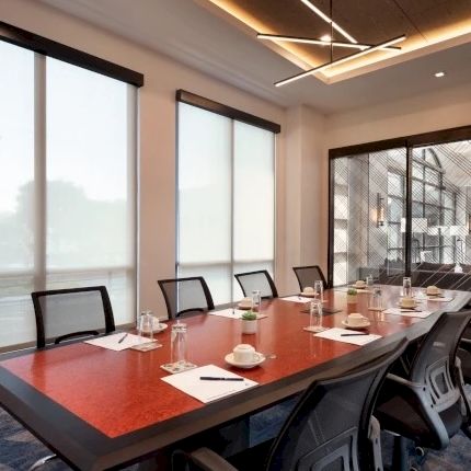 A modern conference room with a long boardroom table, chairs, drinks, and large windows letting in daylight.