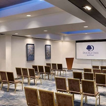 An empty hotel meeting room with rows of chairs and a DoubleTree by Hilton banner on the wall.