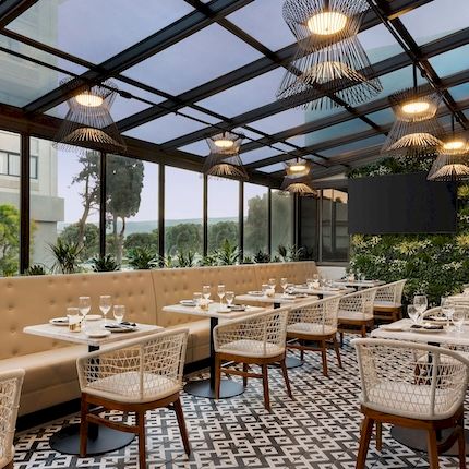 An elegant outdoor dining patio with wicker chairs, neatly set tables, patterned floor tiles, and hanging pendant lights.