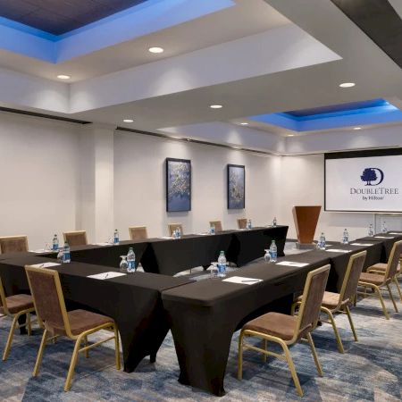 A modern conference room with a long black table, chairs, and a projection screen showing a DoubleTree sign.