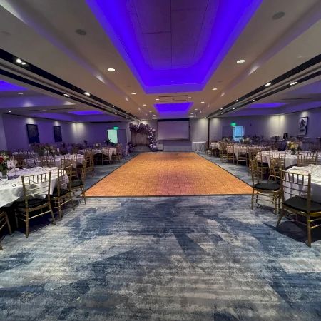 A decorated event banquet hall with blue LED ceiling lights, a central aisle, and rows of gold chairs set for a ceremony.