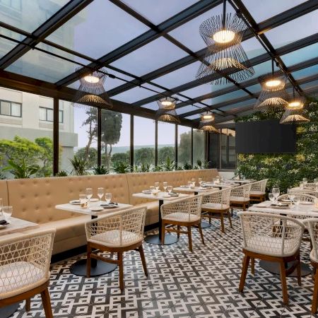 An elegant outdoor dining setup with neatly set tables and wicker chairs under a glass roof.